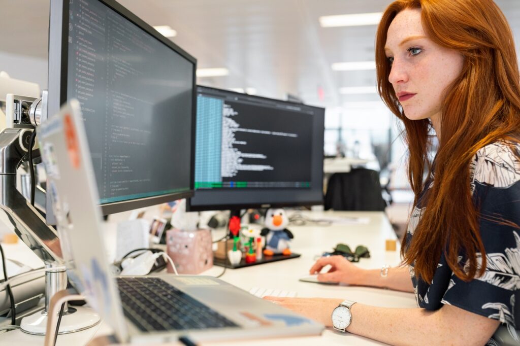 vrouw met rood haar zit achter computer te programmeren