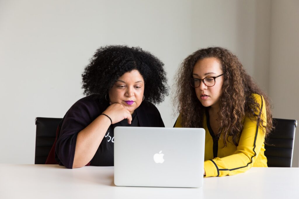 twee vrouwen zitten achter een Apple laptop