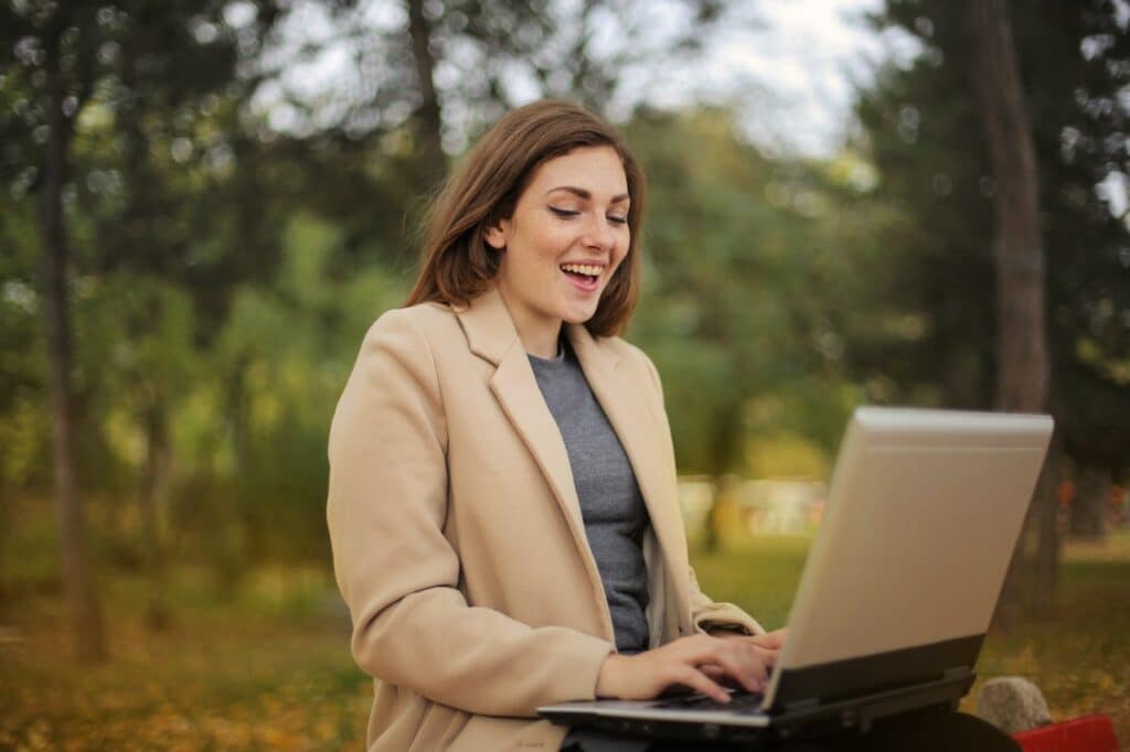 vrouw zit in bos achter laptop en lacht