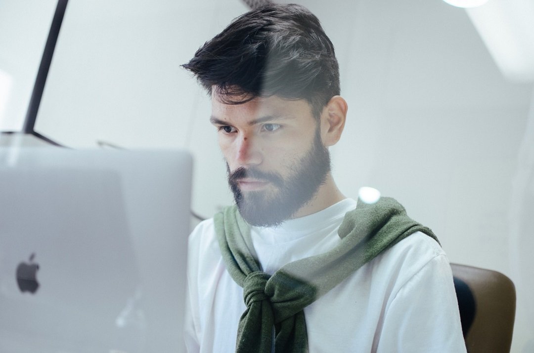 Man met donker haar en donkere baard werkt op een iMac