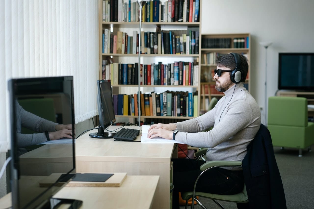 Blinde man met koptelefoon zit achter computer