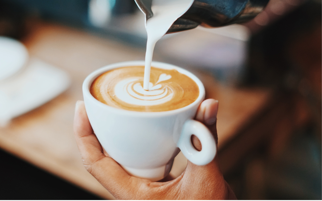 Een barista schenkt melk in een kopje koffie