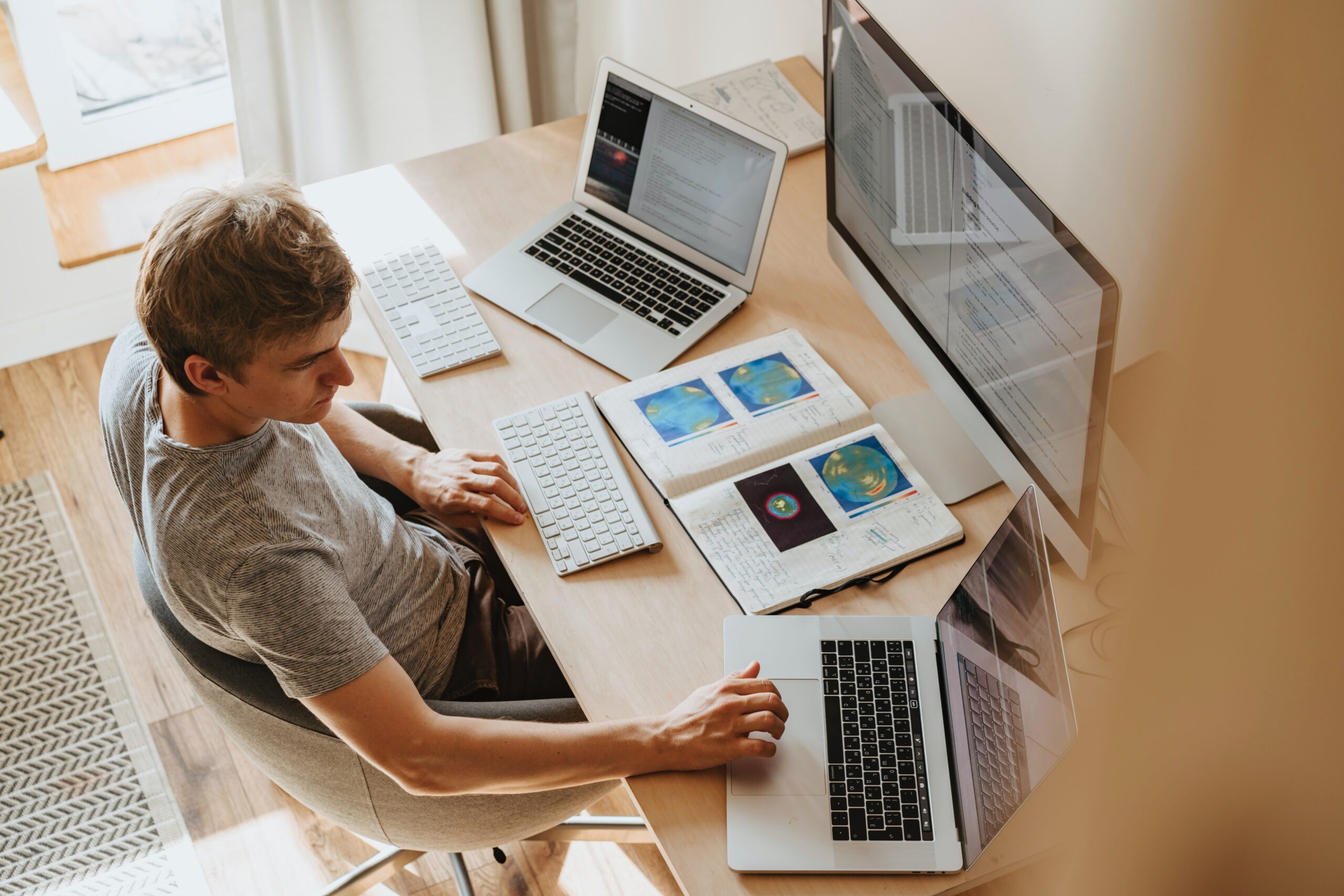 Een webontwikkelaar van bovenaf gefotografeerd, terwijl hij aan zijn bureau zit, omringd door laptops en schermen.