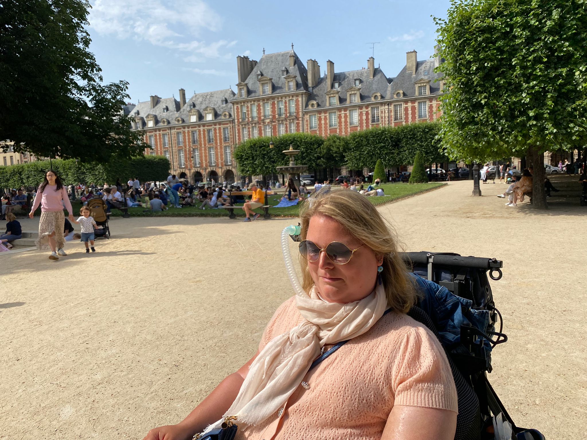 Judith met een zonnebril op in Parijs in een mooi park met een oud gebouw.